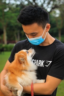 man in black crew neck t-shirt holding brown long coated small dog