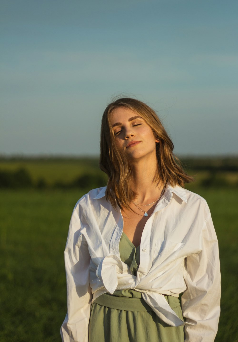 woman in white button up shirt standing on green grass field during daytime