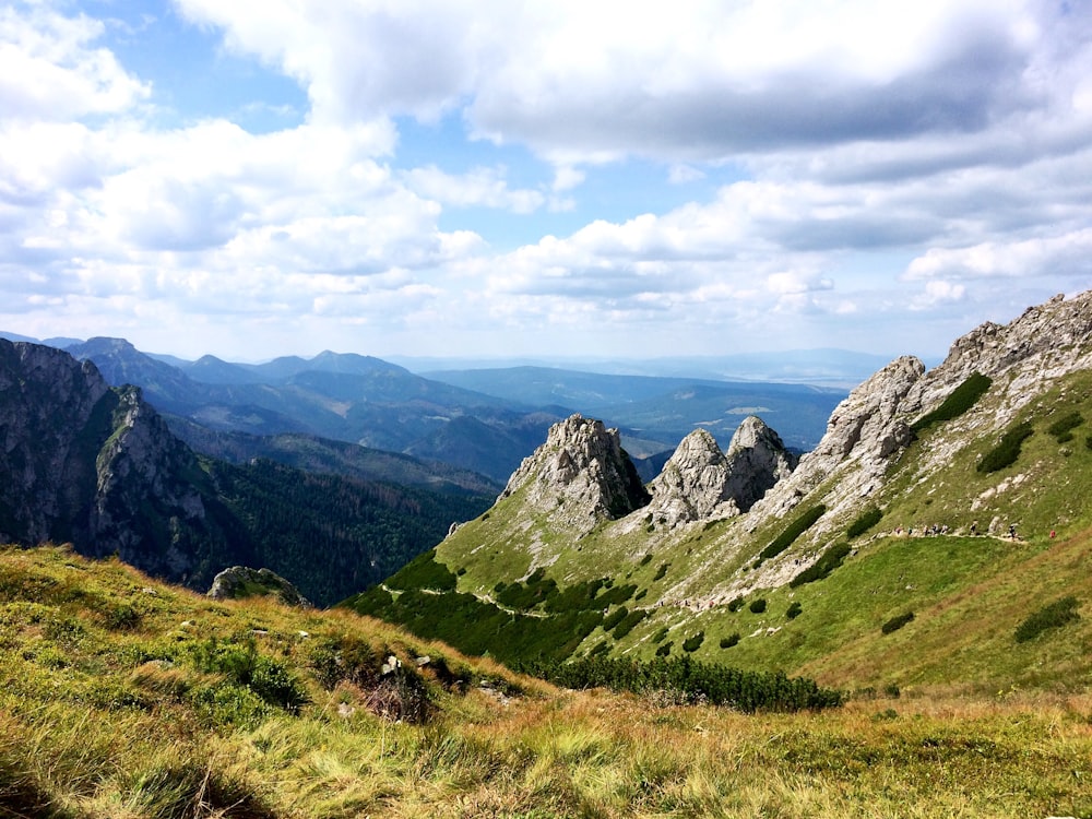 campo de grama verde e montanhas sob nuvens brancas e céu azul durante o dia