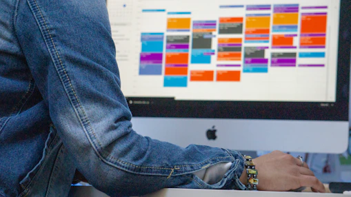 A person in a denim jacket using a computer with a colorful calendar display
