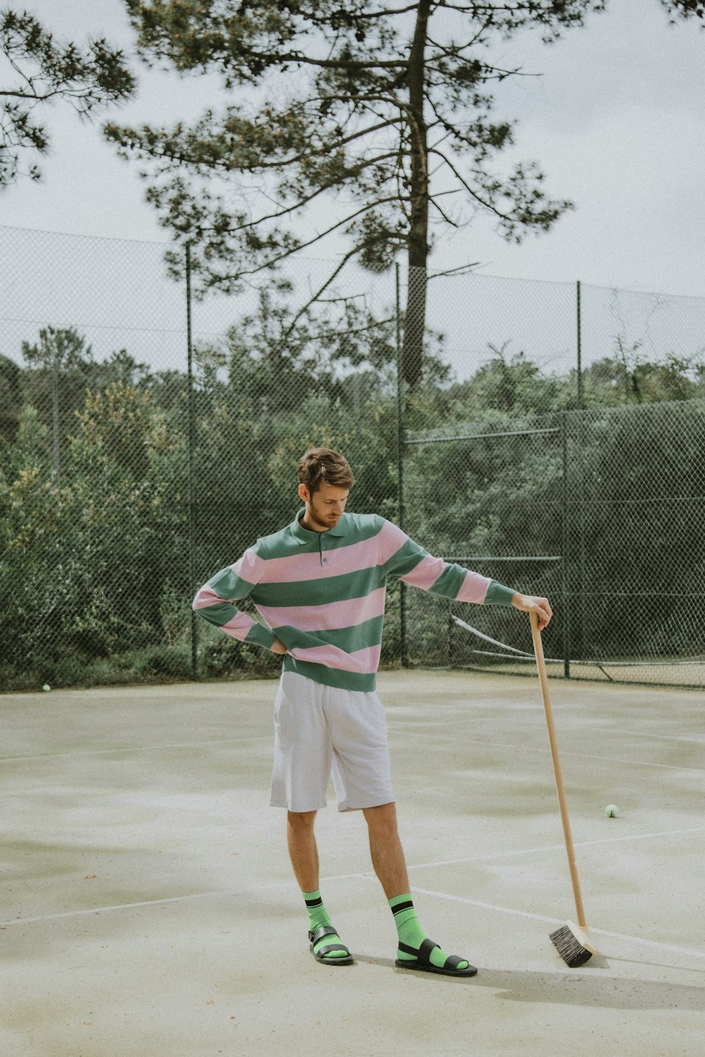 man in red and white stripe polo shirt and white shorts holding brown wooden stick