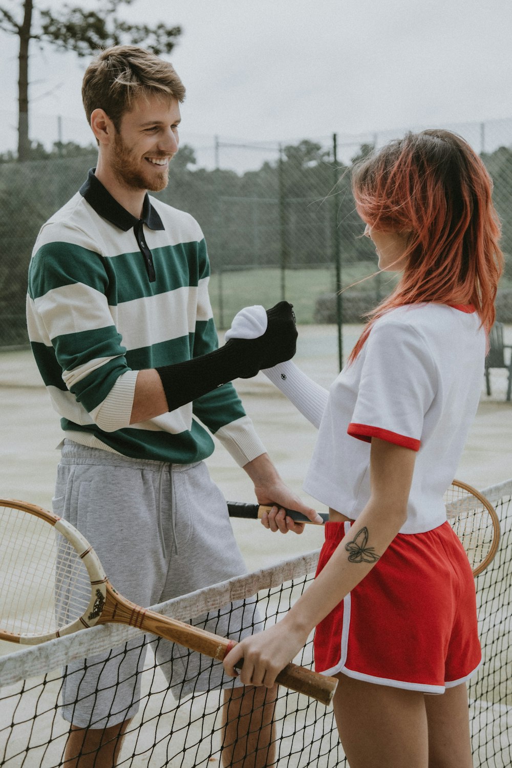 茶色のテニスラケットを持つ白と緑の縞模様のポロシャツを着た男