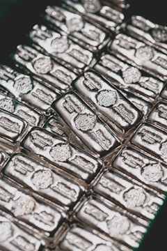 Stacks of shiny silver bars are neatly arranged, each bar featuring engravings and distinctive markings.