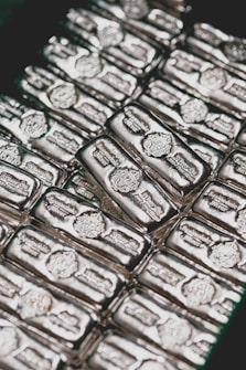 Stacks of shiny silver bars are neatly arranged, each bar featuring engravings and distinctive markings.