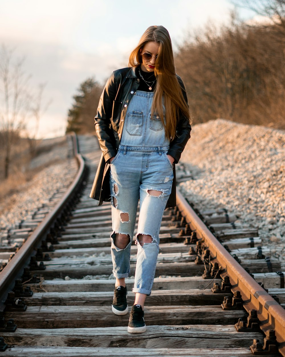 woman in blue denim jacket and blue denim jeans standing on brown wooden train rail during