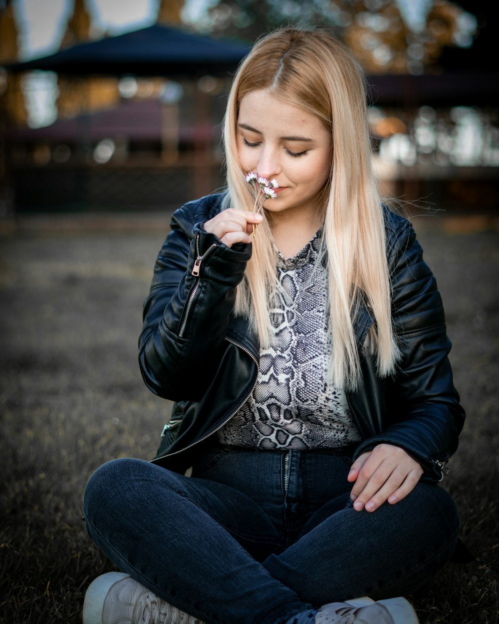 Frau in schwarzer Lederjacke und blauer Jeans sitzt auf dem Boden