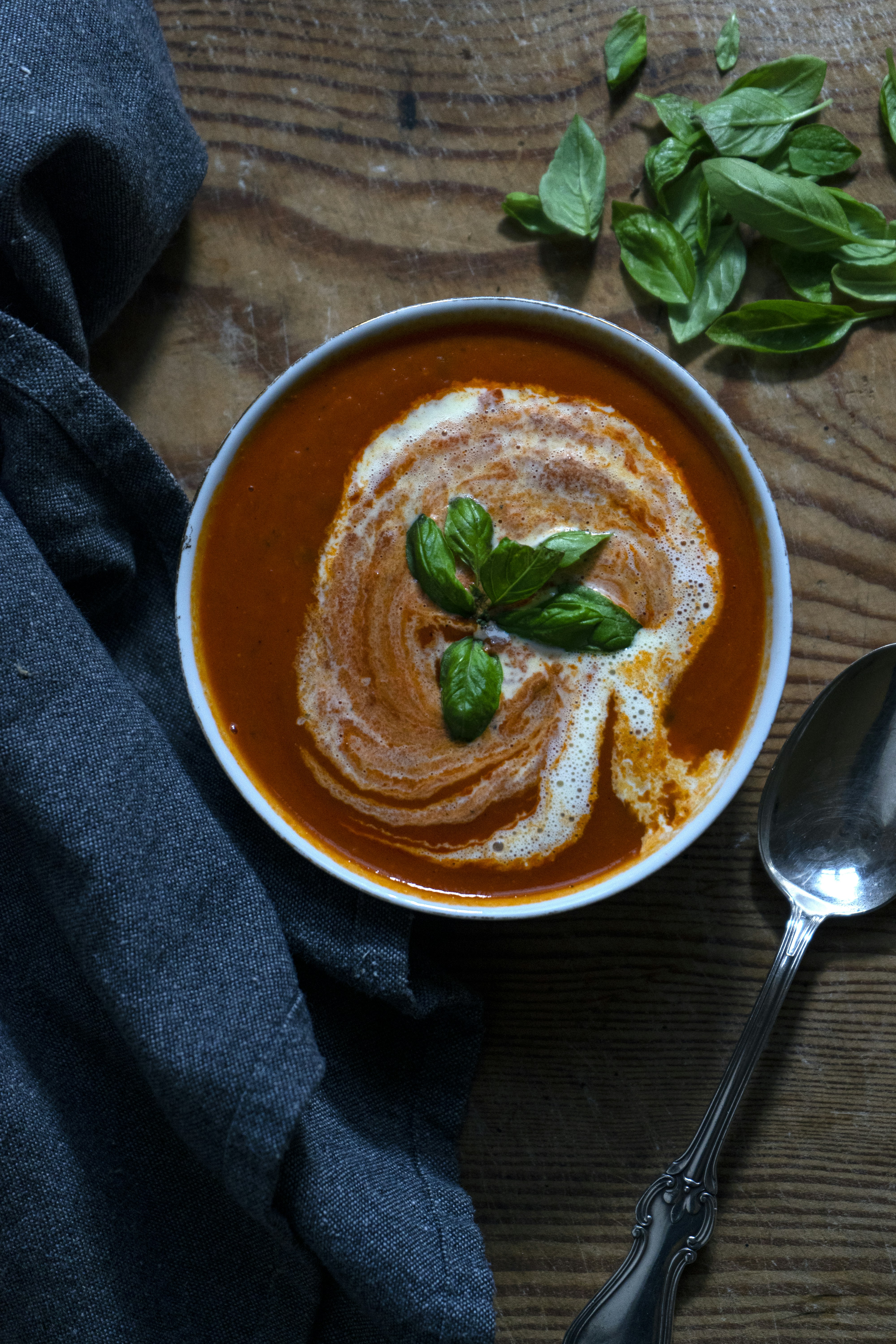 Rich red tomato soup in white bowl with basil garnish and cream swirl