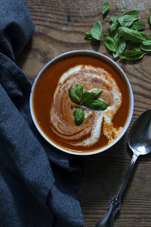 A vibrant bowl of creamy tomato basil soup topped with fresh basil leaves and a drizzle of olive oil.