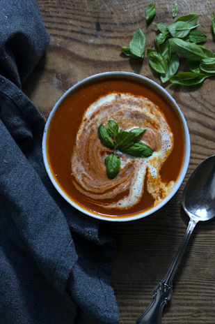 A rustic wooden table set with a steaming bowl of homemade tomato soup garnished with fresh basil.