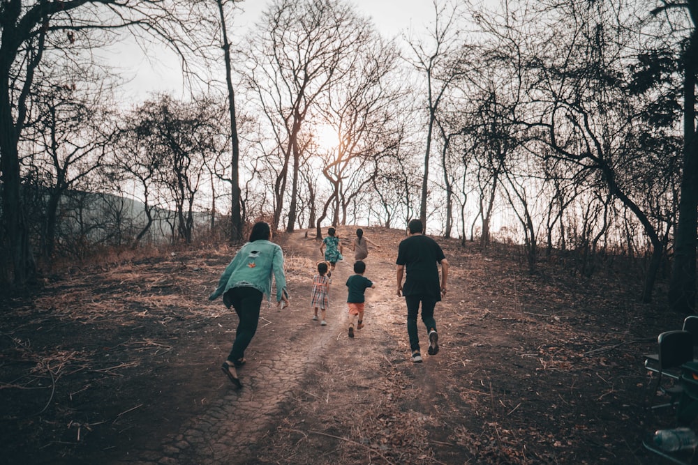 2 women and 2 children walking on brown dirt road between bare trees during daytime