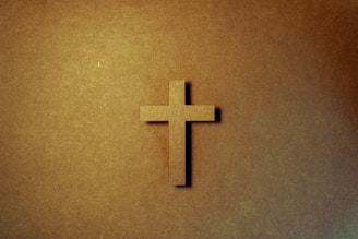 A warm image of hands holding a small wooden cross with soft sunlight in the background.