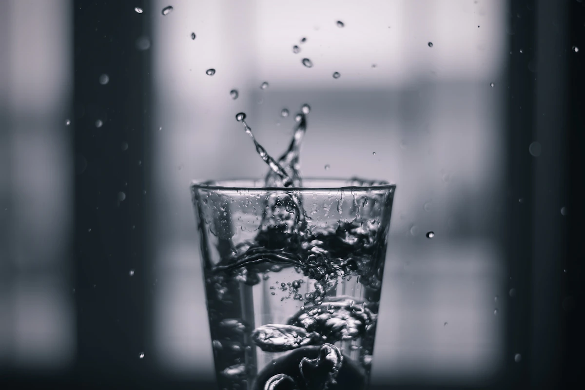 Water pouring into a clear drinking glass that is already full, spilling over the rim, analogous to reasoning tokens added past the point where a model already has the right answer, where the extra pour does not help and can knock the answer over