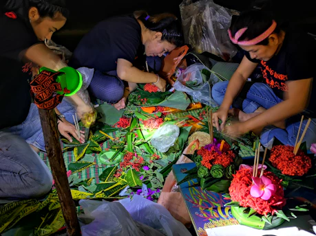A lively workshop with participants creating floral art pieces alongside trajineras on a sunny canal.
