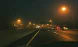 Nighttime highway with a line of trucks moving under streetlights.