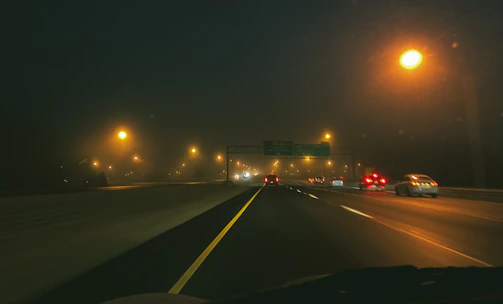 Nighttime highway with a line of trucks moving under streetlights.