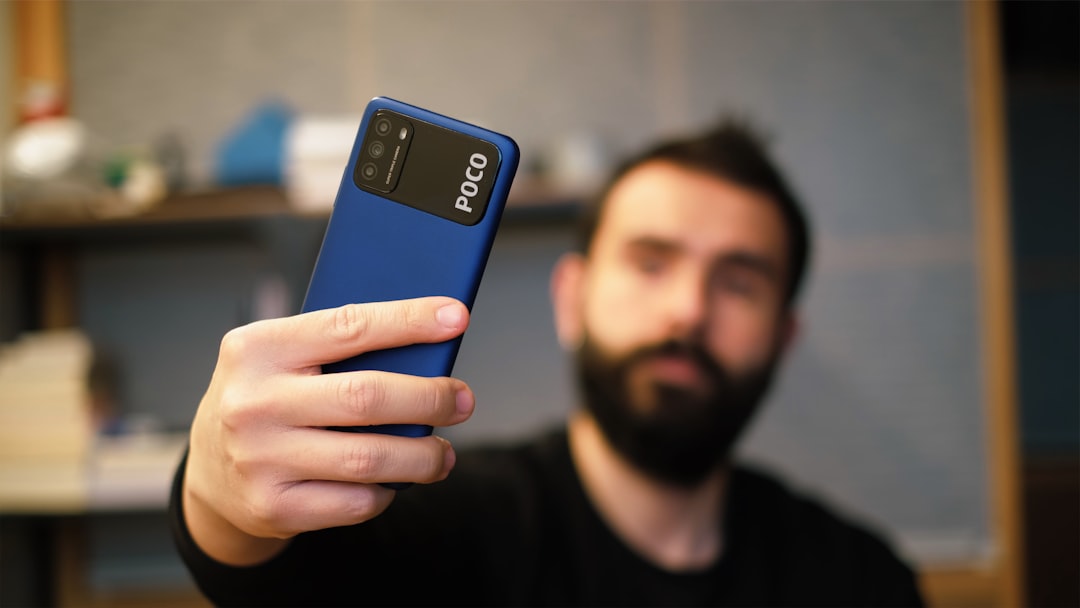 man in black crew neck shirt holding blue samsung android smartphone, Young man taking selfies with mobile phone