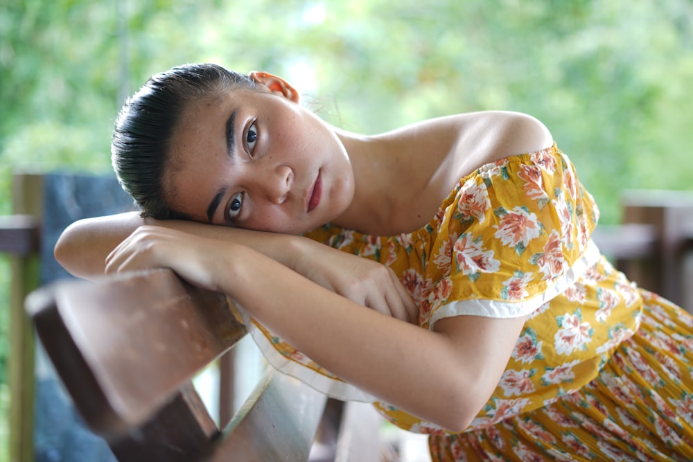 woman in yellow and white floral dress sitting on brown wooden chair