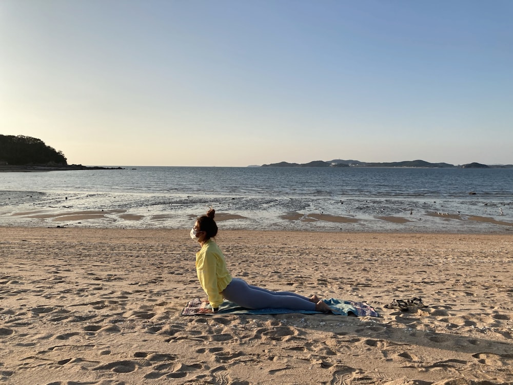 woman in yellow shirt and blue pants sitting on beach shore during daytime