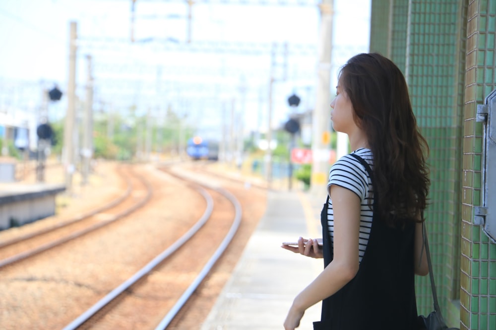 woman in black and white stripe shirt standing on train rail during daytime