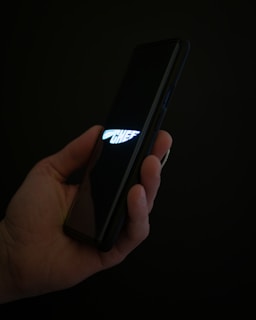 A hand holding a smartphone displaying the word 'CHEF' with a stylized knife logo on a dark screen. The background is dark, emphasizing the glow from the screen.