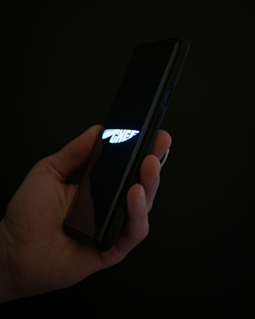 A hand holding a smartphone displaying the word 'CHEF' with a stylized knife logo on a dark screen. The background is dark, emphasizing the glow from the screen.