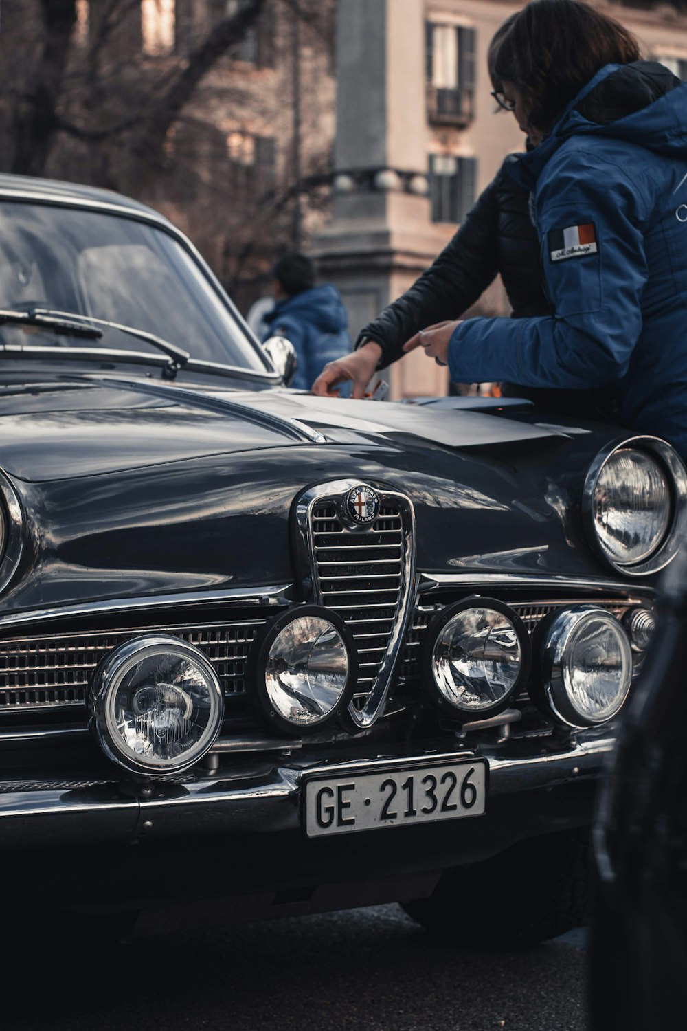 黒い車の脇に立つ黒いスーツのジャケットを着た男