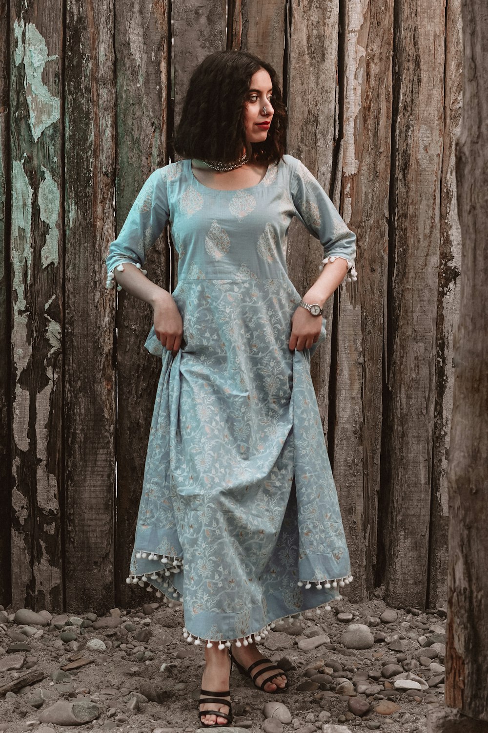 donna in abito blu e bianco in piedi accanto al muro di legno marrone