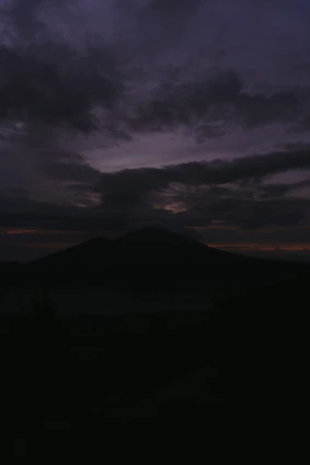 A moody, cinematic portrait of Mike standing against a rugged mountain backdrop at dawn, embodying quiet strength.