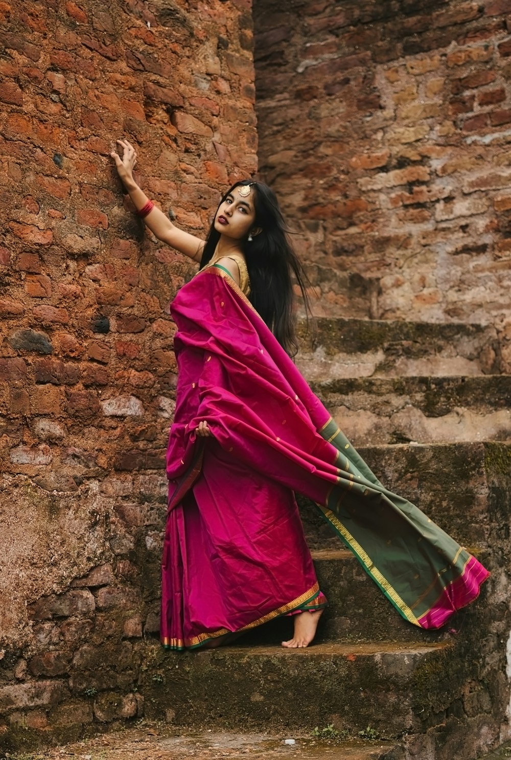 woman in red and purple sari dress leaning on brown brick wall