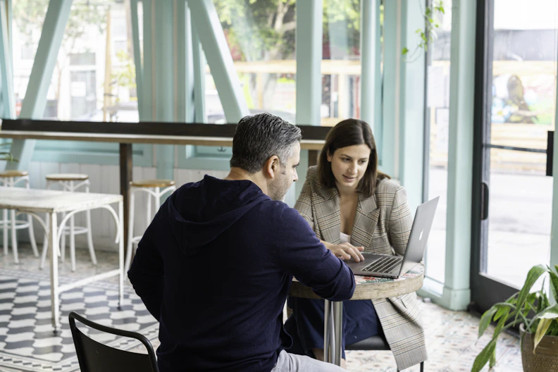 A man and a woman working on a laptop at a cafe table