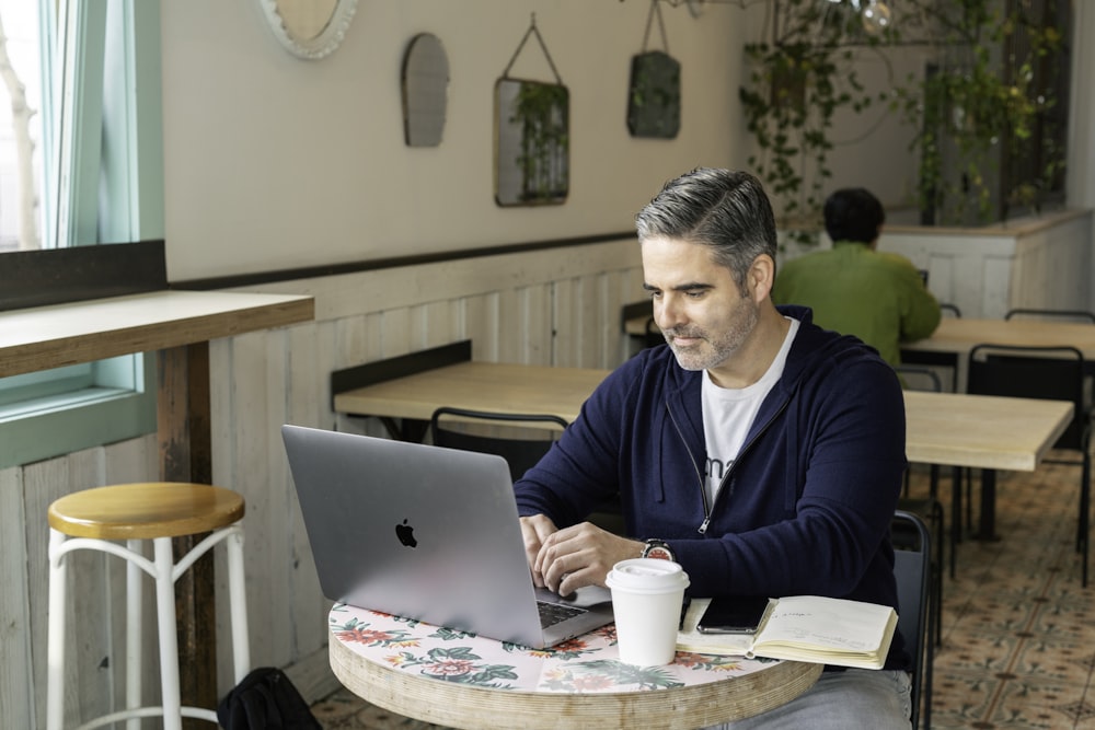 man in blue sweater sitting by the table using macbook