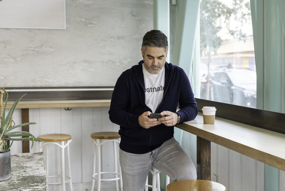 man in blue long sleeve shirt and gray pants holding black smartphone