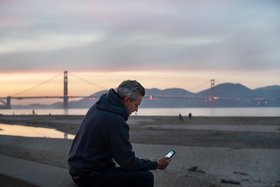 man in black hoodie sitting on gray concrete pavement during daytime