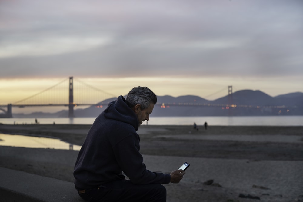 man in black hoodie sitting on gray concrete pavement during daytime