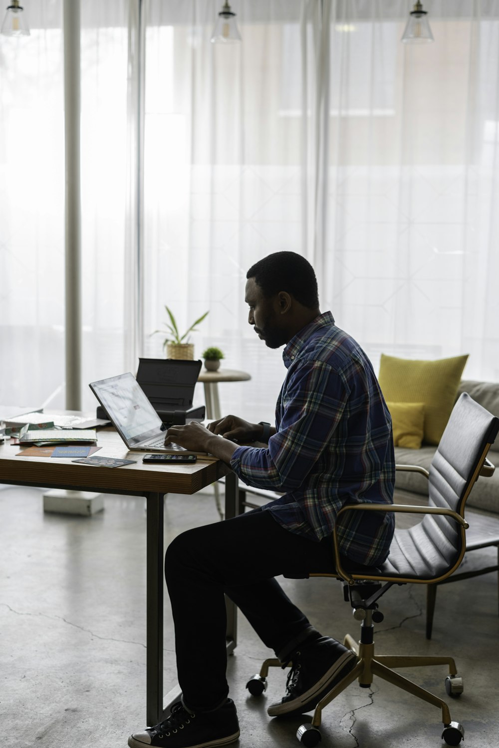 man in blue and white plaid dress shirt sitting on chair using laptop computer