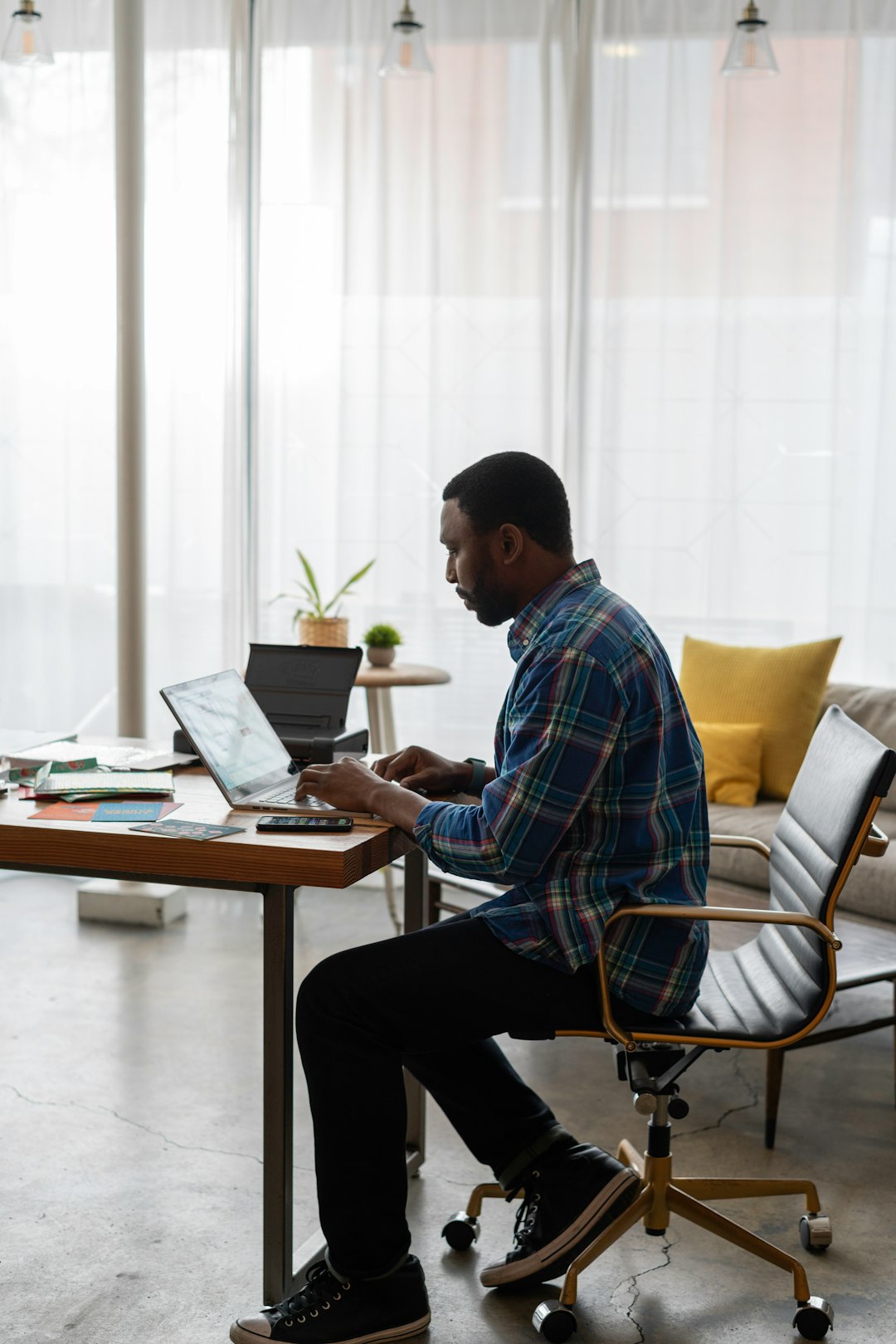 man in blue and white plaid dress shirt sitting on chair using laptop computer