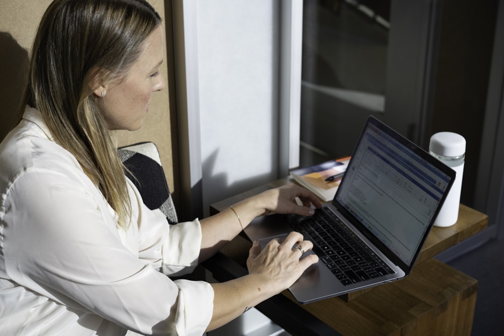 Mujer en camisa blanca de manga larga usando computadora portátil negra