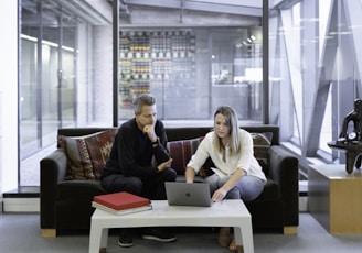 man and woman sitting on couch using macbook