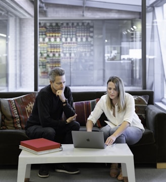 man and woman sitting on couch using macbook