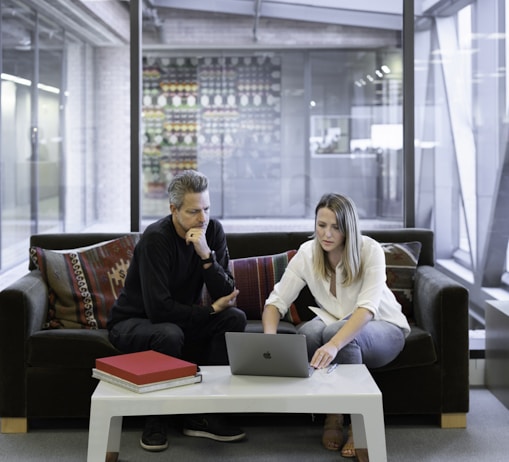 man and woman sitting on couch using macbook