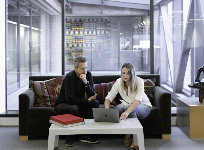 man and woman sitting on couch using macbook