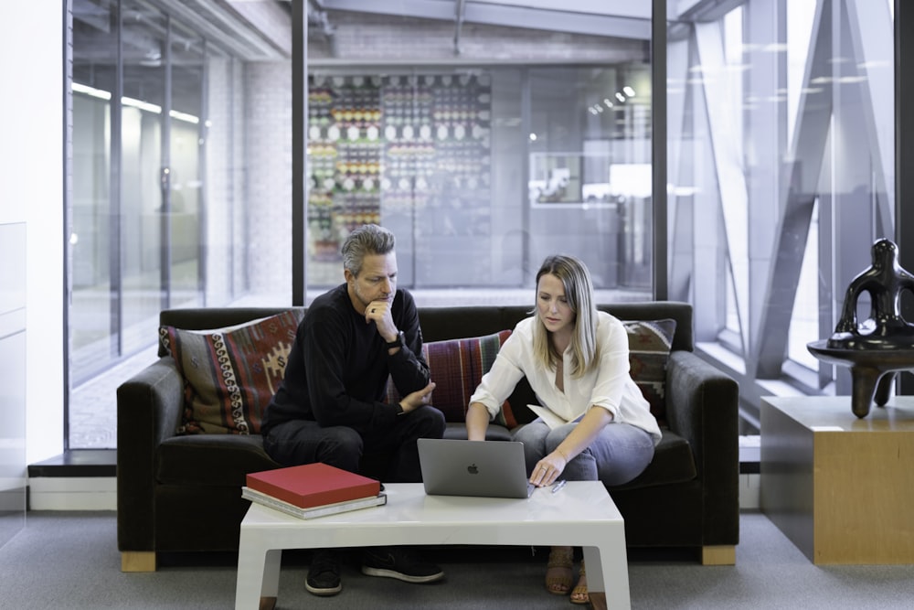 man and woman sitting on couch using macbook