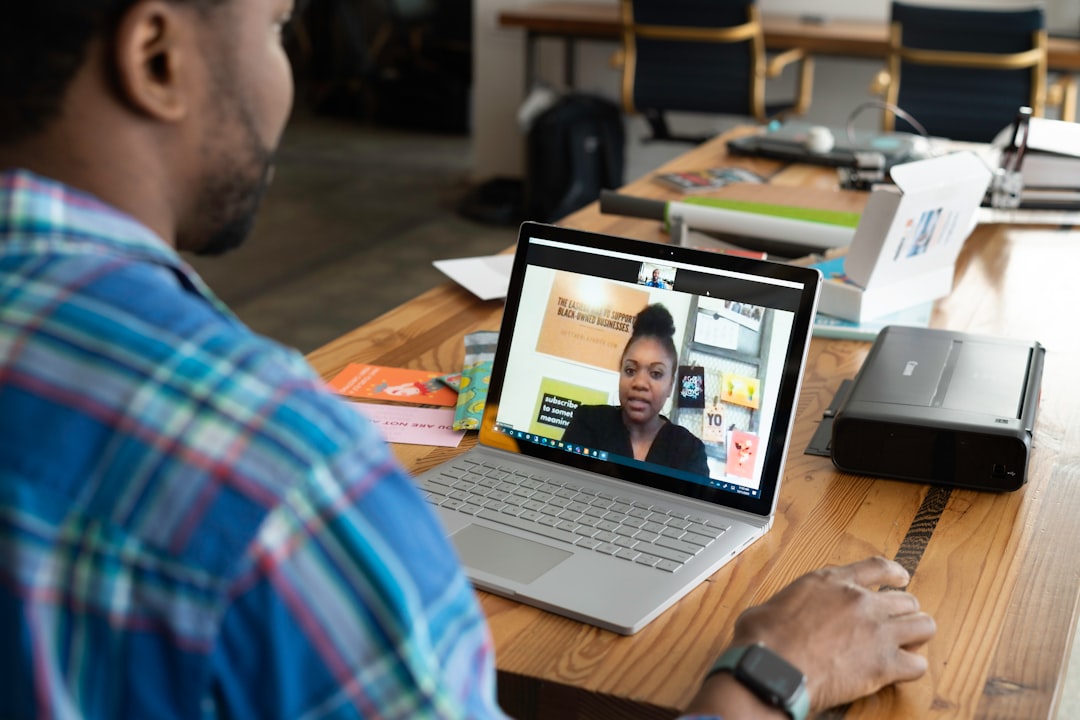 man in blue and white plaid shirt using macbook pro, A salesperson working in an office on a virtual call
