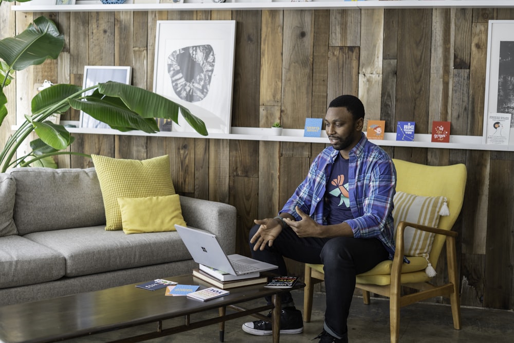 man in blue and white plaid dress shirt and black pants sitting on couch using macbook