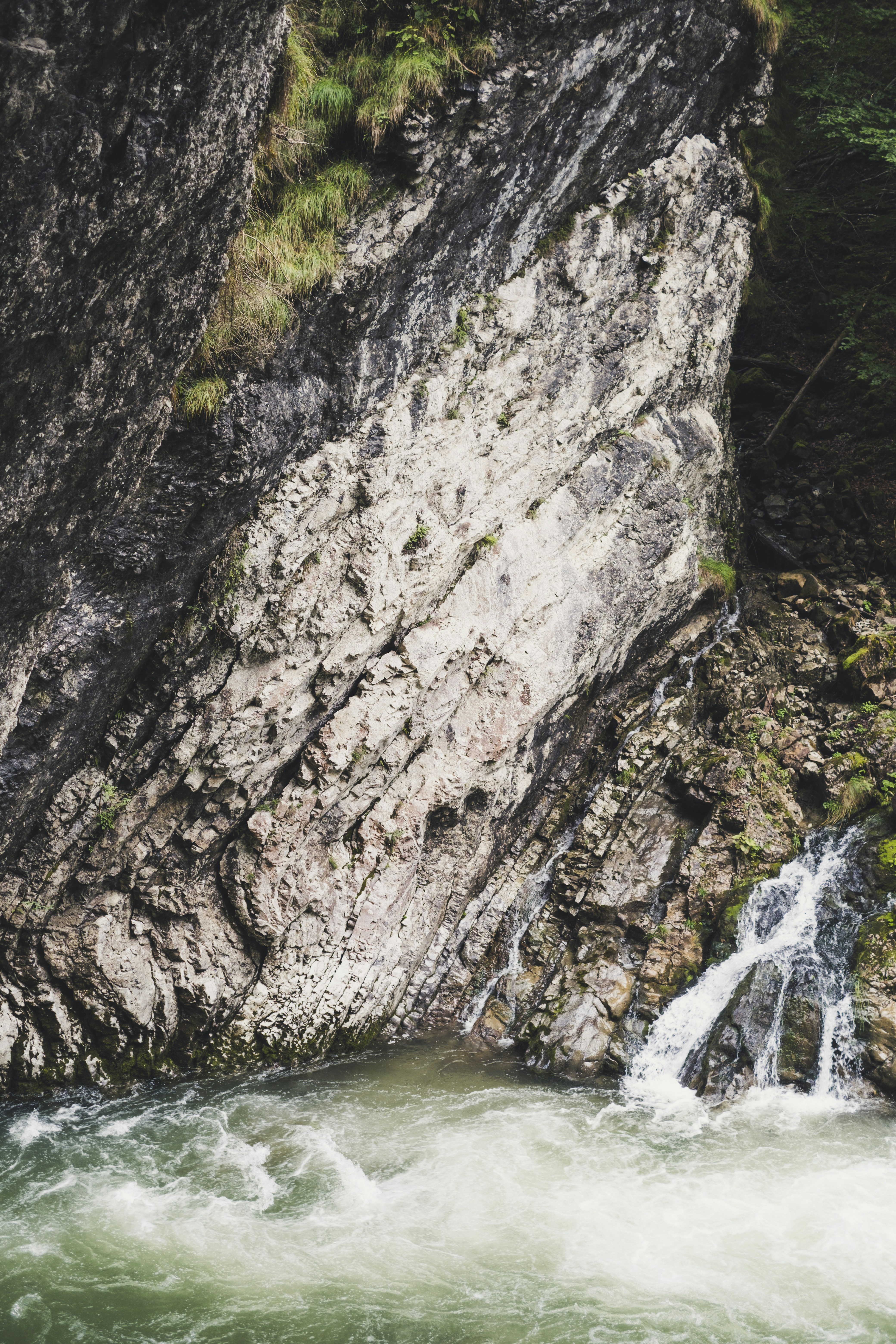 water falls between gray and green rocky mountain during daytime