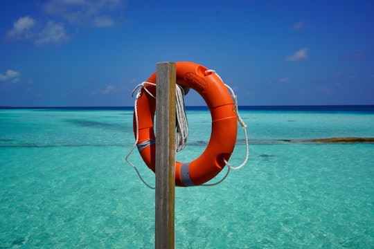 orange and white life buoy hanged on brown wooden post during daytime in Alif Alif Atoll Maldives