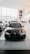 A sleek black car with a shiny, modern design is prominently displayed in a spacious and well-lit showroom. The showroom features large windows allowing natural light to pour in, highlighting the vehicle's features. Other cars are lined up in the background along the sides.