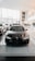 A sleek black car with a shiny, modern design is prominently displayed in a spacious and well-lit showroom. The showroom features large windows allowing natural light to pour in, highlighting the vehicle's features. Other cars are lined up in the background along the sides.