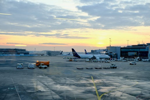 A bustling airport runway at sunset with planes taxiing and taking off.