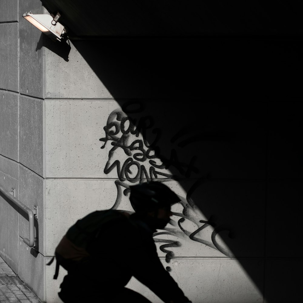 man in black jacket and black cap standing beside wall during daytime